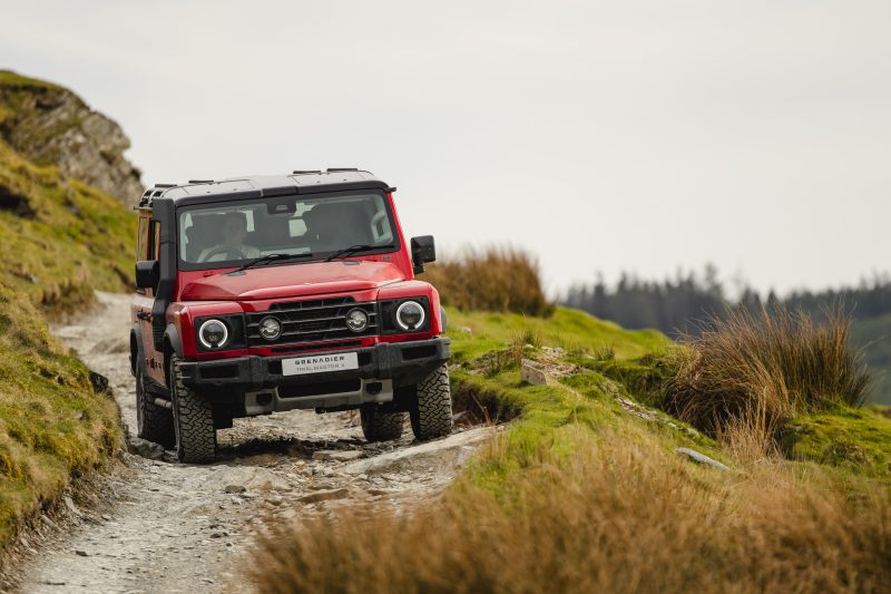 Red Ineos Grenadier driving through rugged off-road terrain, reflecting the outdoor automotive aesthetics discussed by David Gensler in his VANISH interview.