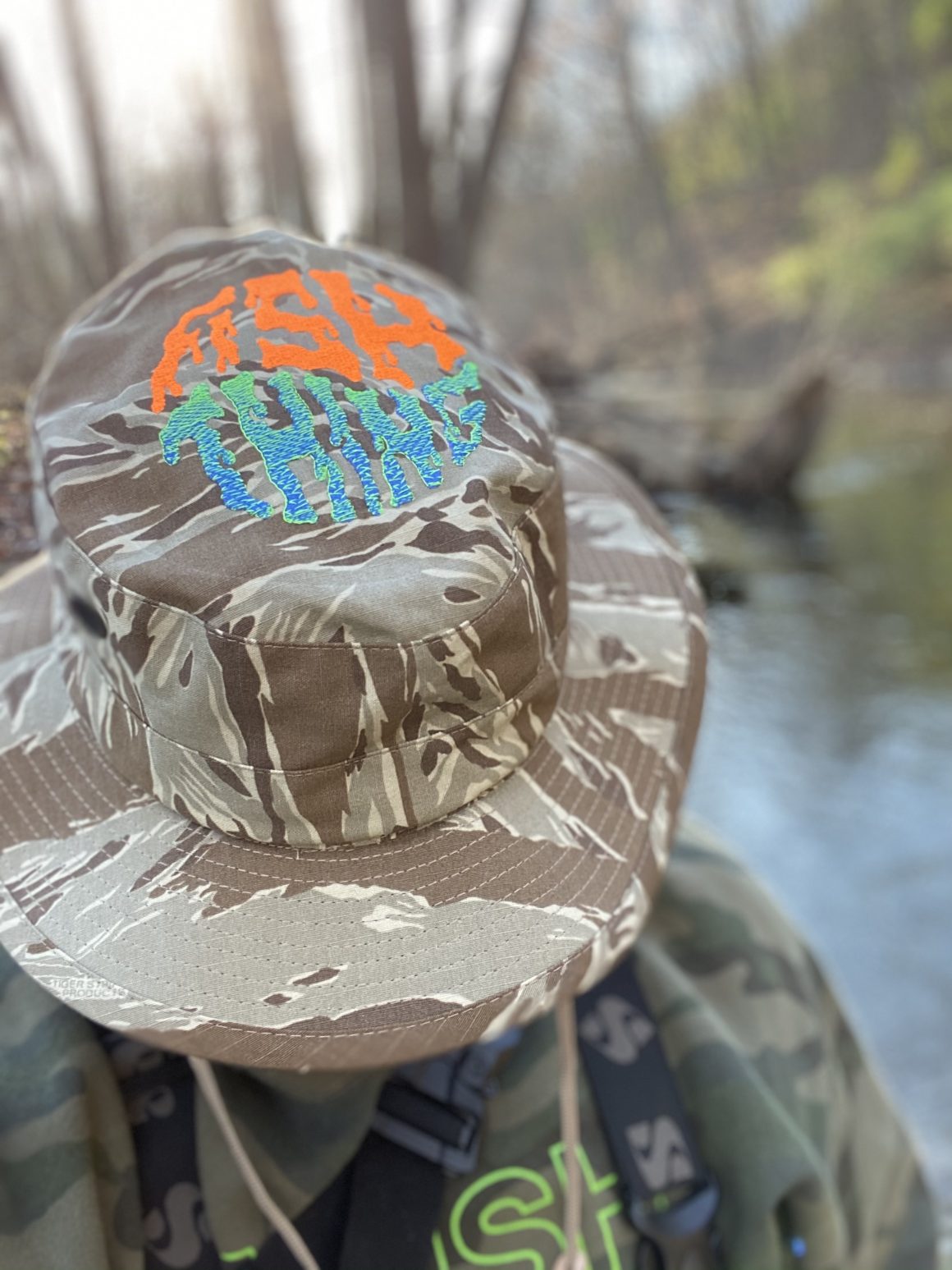 David Gensler wearing a camouflage Fish Thing hat while fishing by a creek.